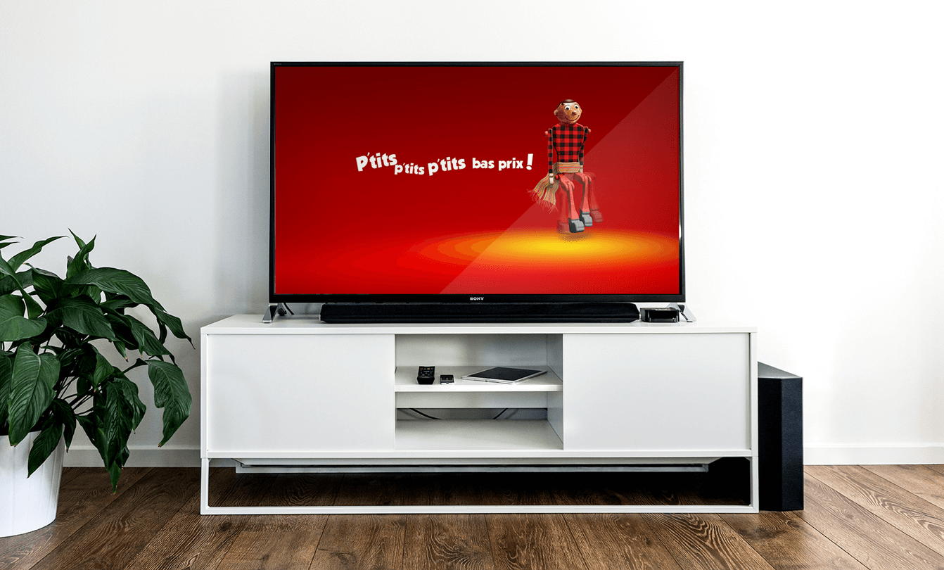 Un salon moderne avec grand écran de télévision montrant une publicité Economax, un écran rouge avec un pantin habillé québécois dansant le rigodon et écrit p'tits, p'tits, p'tits bas prix!