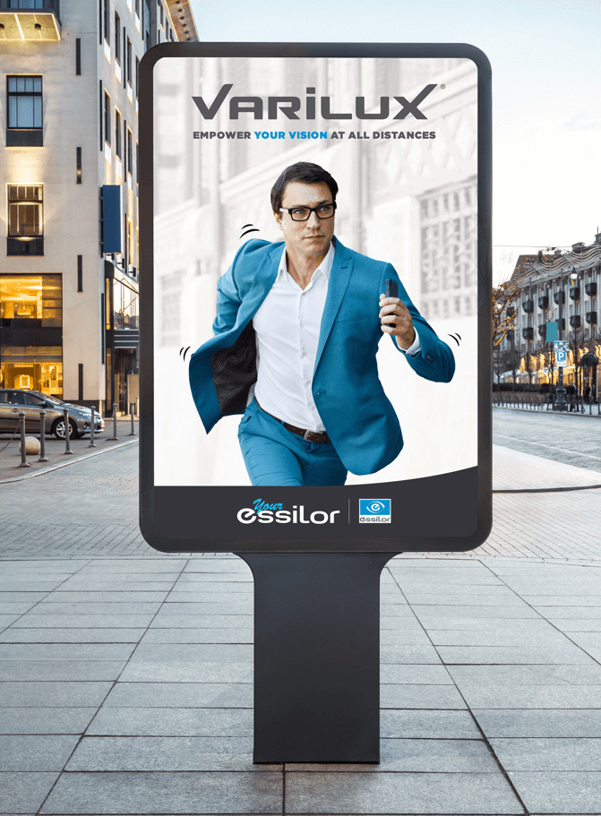 Panneau sur le bord de la route avec publicité Varilux un homme avec des lunettes qui court en veston bleu ciel et slogan Empower your vision at all distances